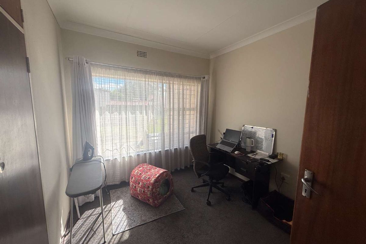 A functional bedroom featuring neutral walls, carpeting, and a large window providing natural light, suitable for use as a home office or guest room.