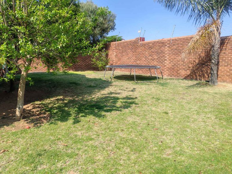 A private rear garden featuring a well-maintained lawn, established trees, and secure brick boundary walls topped with electric fencing.