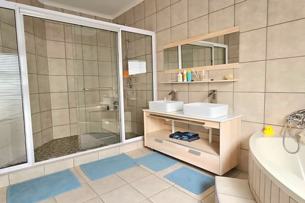 A spacious bathroom featuring a large walk-in glass shower, a double vanity with vessel sinks, and a built-in corner bathtub with tiled surround.
