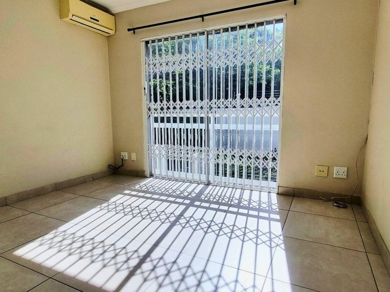 An empty living room featuring tiled flooring, a wall-mounted air conditioning unit, and a sliding glass door with a security gate.