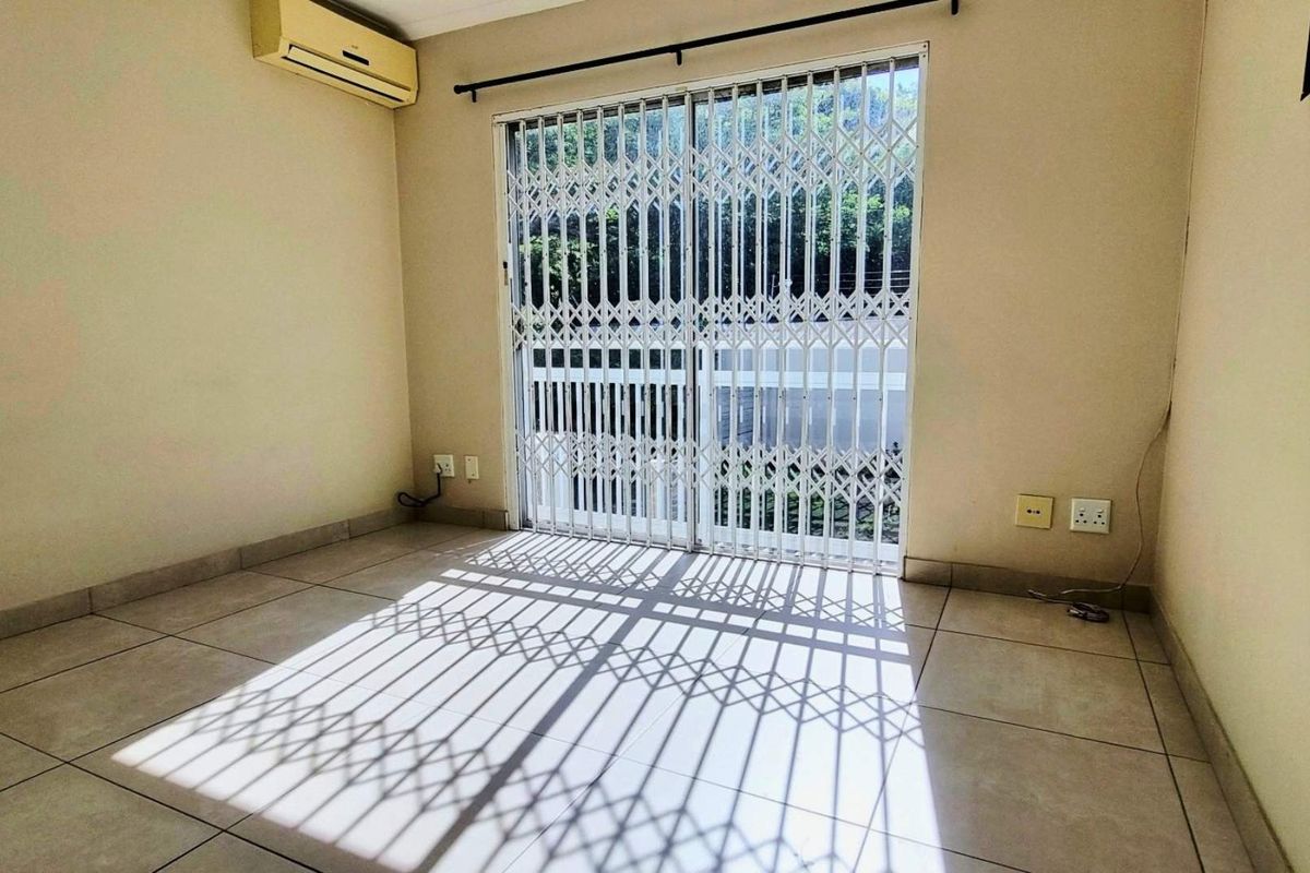 An empty living room featuring tiled flooring, a wall-mounted air conditioning unit, and a sliding glass door with a security gate.