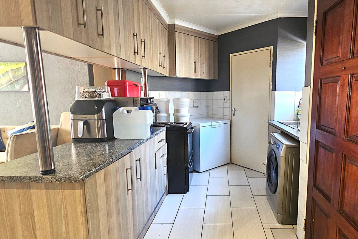 Functional kitchen featuring wood-look cabinetry, granite countertops, tiled flooring, and integrated laundry plumbing, offering a practical layout for daily meal preparation.