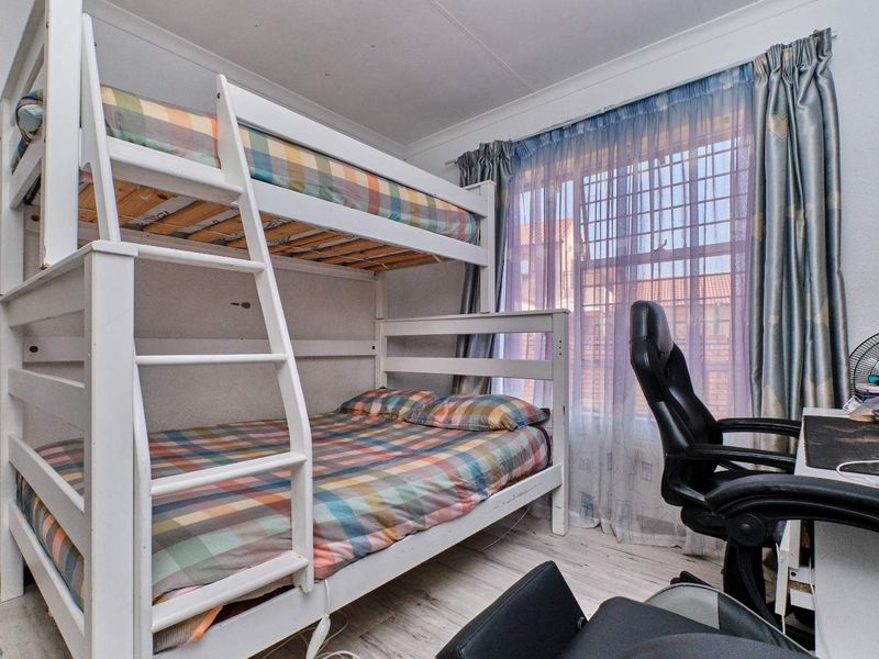 A functional bedroom featuring laminate flooring and security bars on the window, providing a practical space for rest or study.