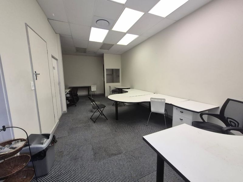 A functional office space featuring a suspended ceiling with recessed lighting, carpeted flooring, and an internal window, suitable for a professional work environment.
