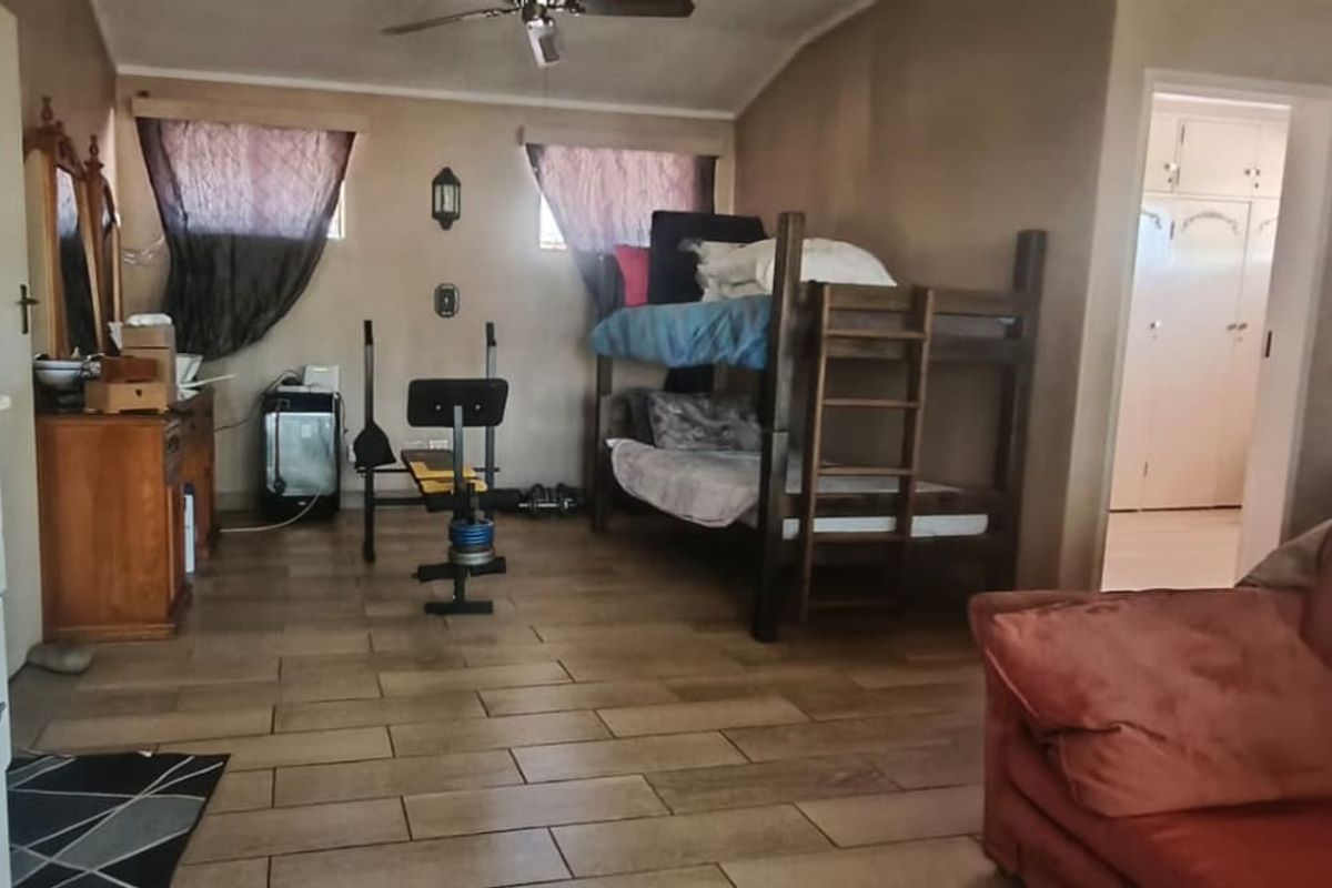 A spacious bedroom featuring tiled flooring, a ceiling fan, and access to an adjoining room with built-in storage cabinetry.