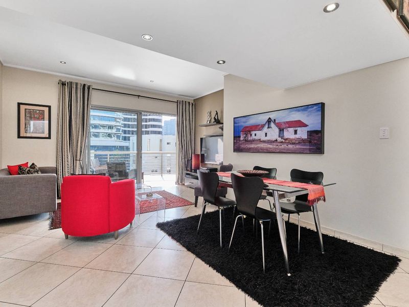 Open-plan living and dining area featuring tiled flooring, recessed downlighting, and large sliding glass doors leading to a private balcony.