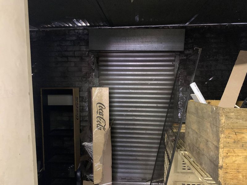 A utility or storage area featuring an exposed brick wall, a metal roller shutter door, and a suspended ceiling grid.