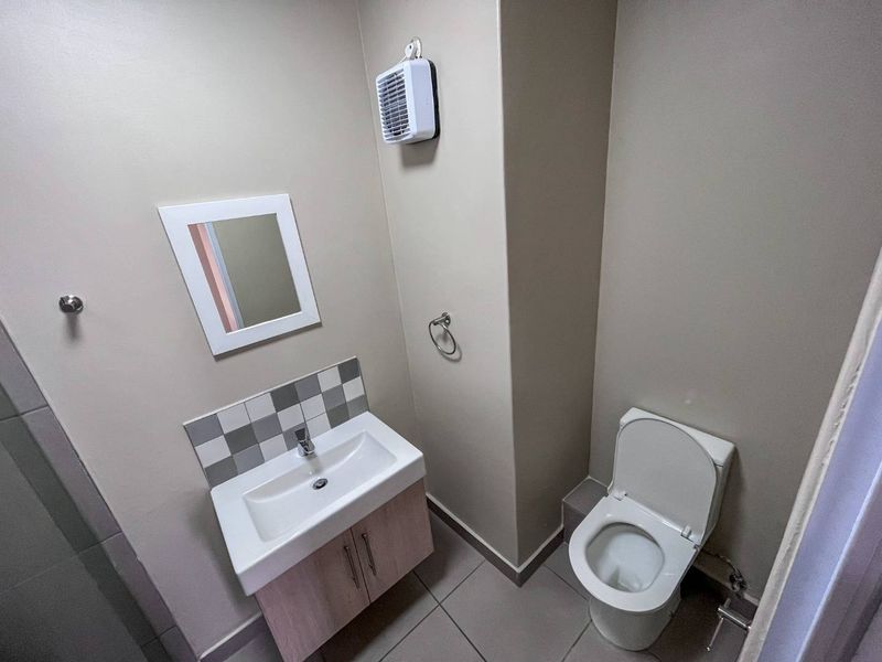 A clean and functional bathroom featuring a modern vanity with basin, tiled splashback, and a wall-mounted extractor fan.