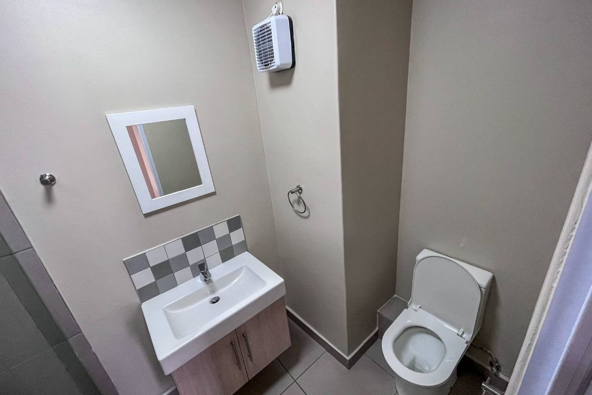 A clean and functional bathroom featuring a modern vanity with basin, tiled splashback, and a wall-mounted extractor fan.