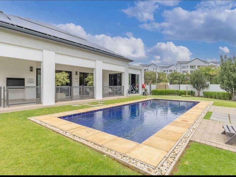 Well-maintained communal pool area featuring a paved surround, landscaped garden, and a covered patio with built-in braai facilities.