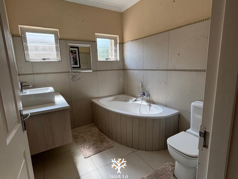 A functional bathroom featuring a built-in bathtub, vessel sink on a vanity cabinet, and a toilet, finished with neutral wall and floor tiles.