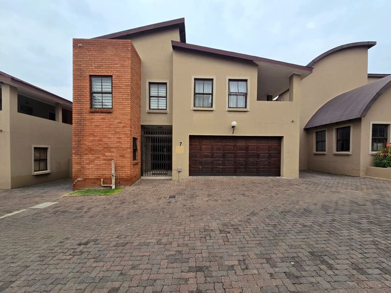 Front elevation of a townhouse featuring a brick facade, paved driveway, and integrated double garage with secure entrance gate.