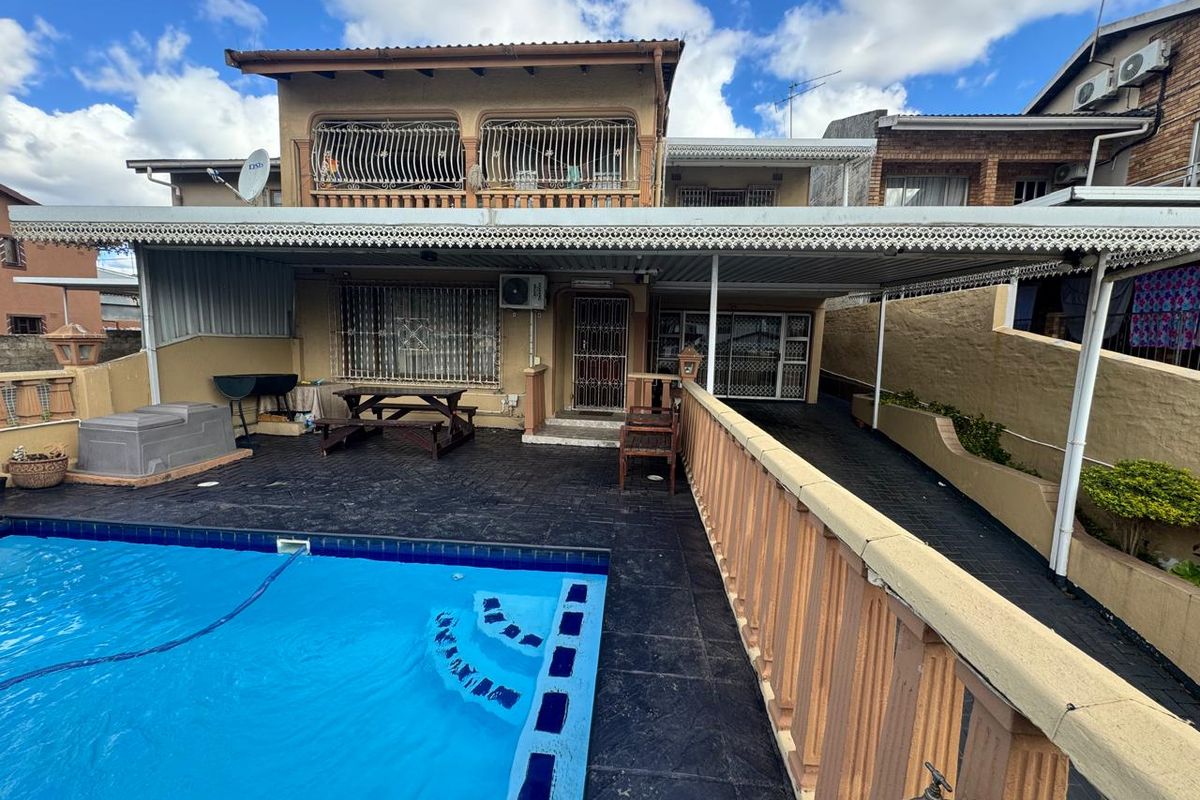 Rear exterior view featuring a swimming pool, a large covered patio area, and a multi-level building facade with security features.