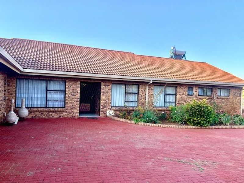 Front elevation of a single-story brick house featuring a tiled roof, solar water heating system, and a spacious paved driveway.