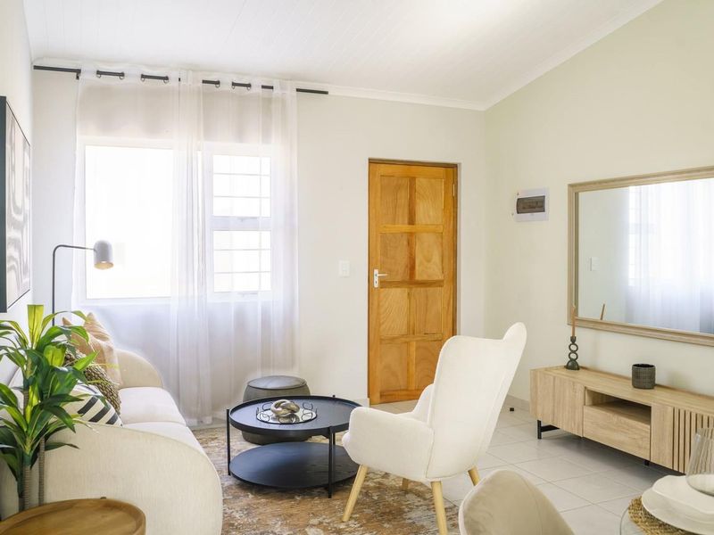 A bright and well-maintained living room featuring tiled flooring, a timber door, and natural light through a large window.