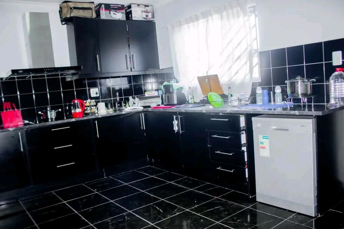 A functional kitchen featuring black cabinetry, contrasting tiled splashbacks, dark floor tiles, and a built-in extractor fan.