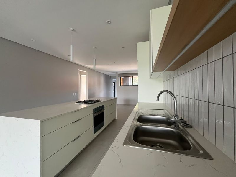 Modern, minimalist kitchen featuring a large island with a built-in oven and gas hob, complemented by stone countertops and a sleek tiled backsplash.