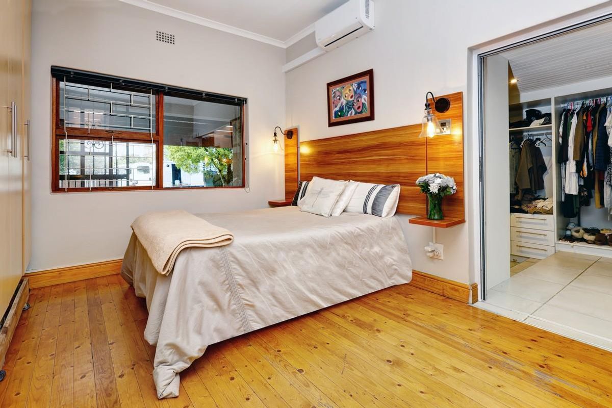 A well-maintained bedroom featuring polished wooden floors, a custom wooden headboard with integrated lighting, air conditioning, and an adjoining walk-in closet.