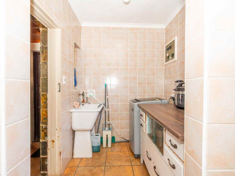 A functional laundry area featuring tiled walls and floors, a utility sink, and built-in cabinetry with a laminate countertop.