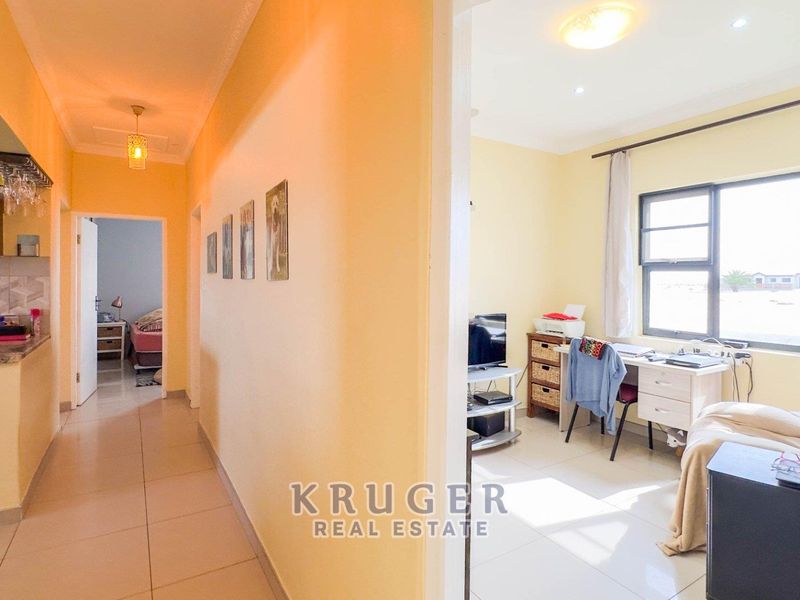 A view from the hallway looking into a home office space, featuring tiled flooring and access to the kitchen area.