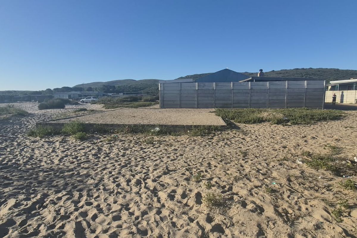 Vacant residential land featuring a concrete slab foundation and perimeter boundary wall, situated in a coastal or sandy environment.
