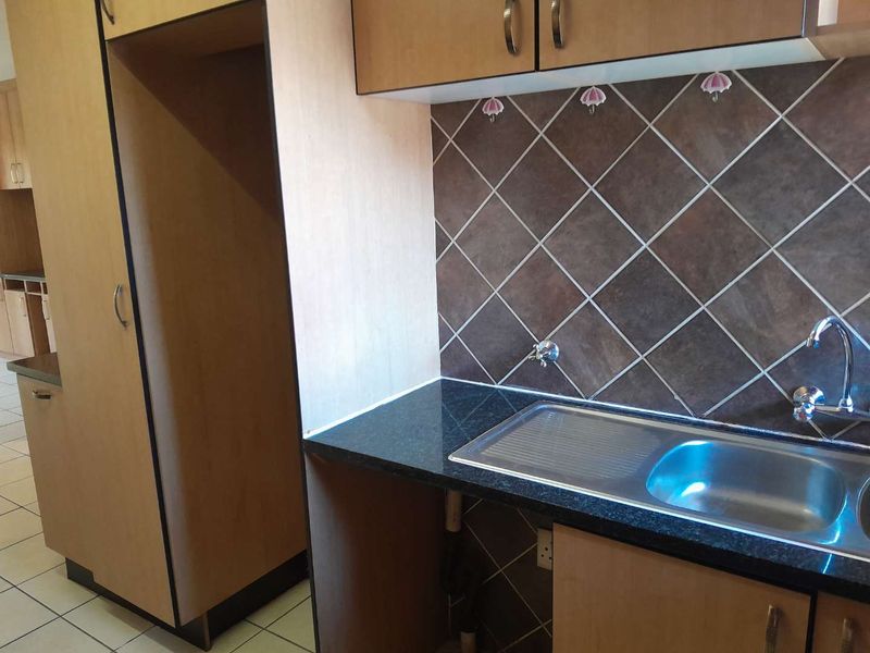 A functional kitchen area featuring laminate cabinetry, granite countertops, a stainless steel sink, and a tiled backsplash.