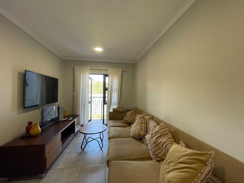 A functional living room featuring tiled flooring, neutral wall tones, and a sliding glass door providing access to an outdoor balcony area.