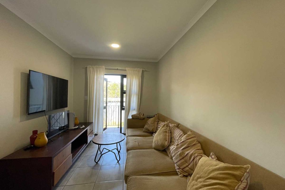 A functional living room featuring tiled flooring, neutral wall tones, and a sliding glass door providing access to an outdoor balcony area.