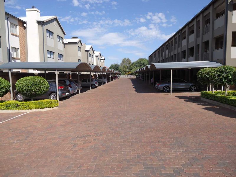 A well-maintained apartment complex parking area featuring covered parking bays, paved driveway, and neat landscaped garden borders.