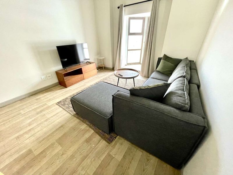 A bright and well-maintained living room featuring light-toned laminate flooring and a large window with curtain tracks.