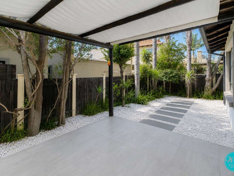 A well-maintained outdoor patio area featuring tiled flooring, a timber pergola with shade cover, and a landscaped garden with stone pathways.