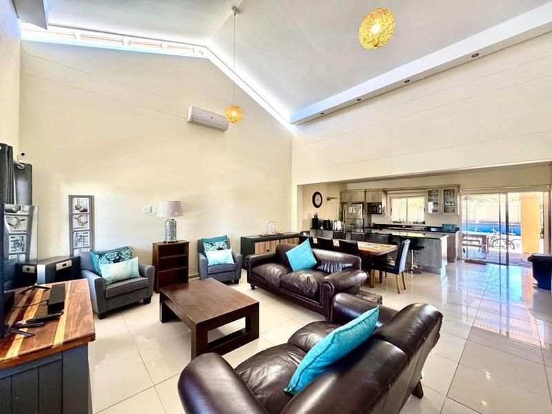 Spacious open-plan living and dining area featuring high vaulted ceilings, modern tiled flooring, and a seamless transition to the kitchen and outdoor patio.