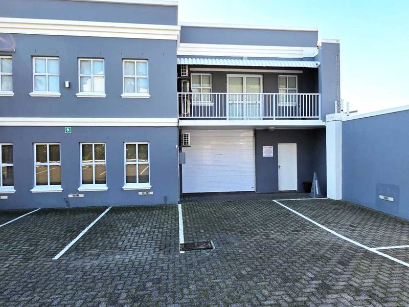Front exterior view of an industrial property featuring a paved parking area, roller shutter door access, and a balcony on the upper level.