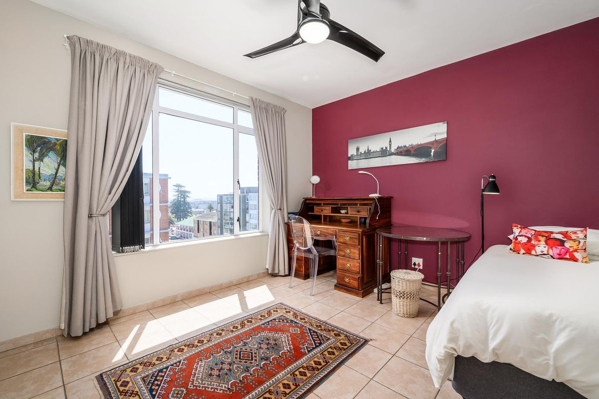 A bright bedroom featuring large windows with city views, tiled flooring, and a modern ceiling fan.