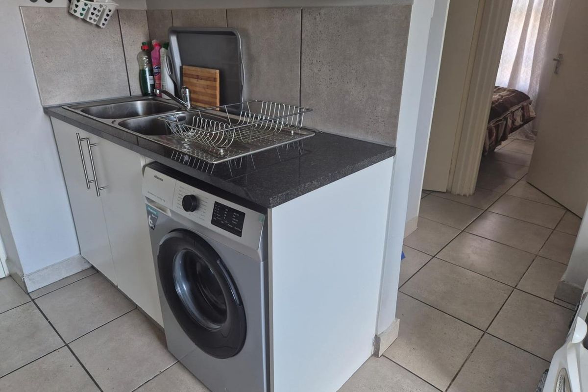 Compact kitchen area featuring a stainless steel sink, stone-look countertop, tiled backsplash, and an integrated washing machine space.