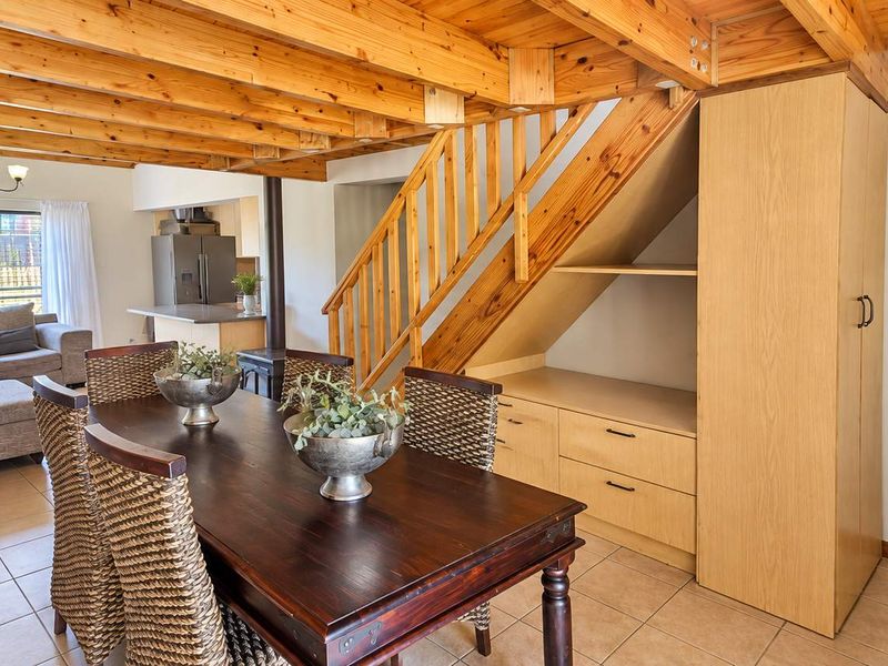 Open-plan living and dining area featuring exposed timber ceiling beams, a wooden staircase with built-in storage, and tiled flooring throughout.