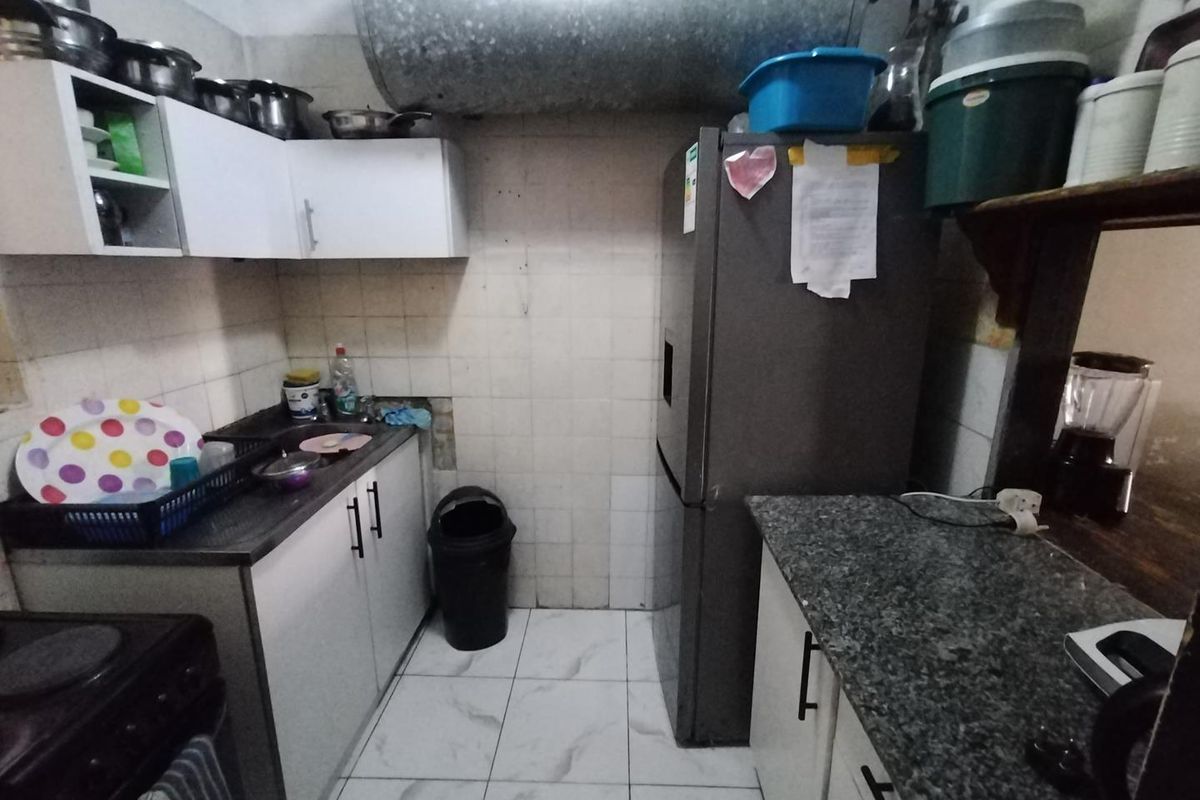 Compact kitchen featuring white cabinetry, granite-look countertops, tiled flooring, and exposed overhead plumbing infrastructure.