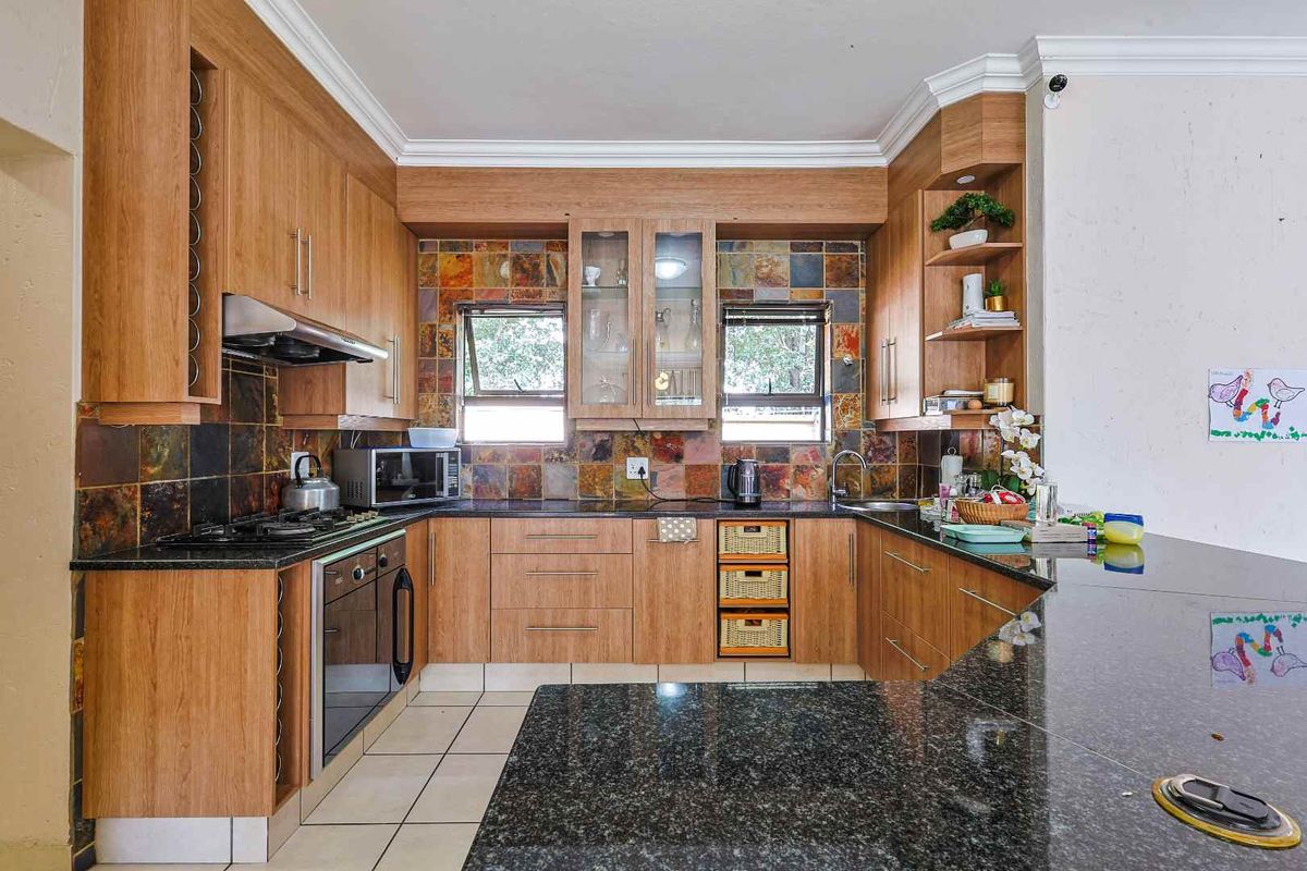 A functional kitchen featuring wood-look cabinetry, granite countertops, a built-in oven, gas hob, extractor fan, and decorative slate tile backsplash.