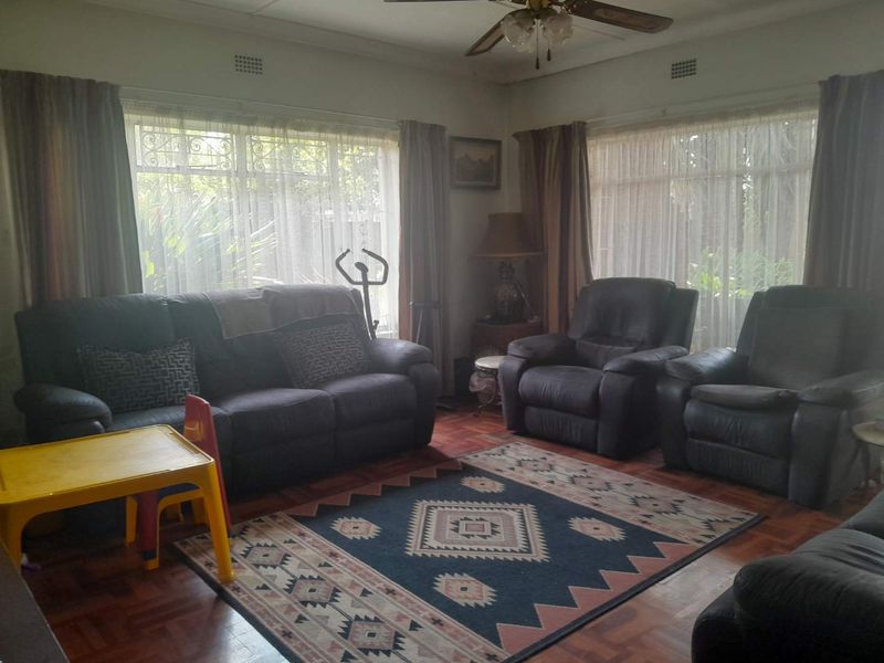 A living room featuring traditional parquet flooring, ceiling fan, and large windows with security bars, offering a classic foundation for updates.