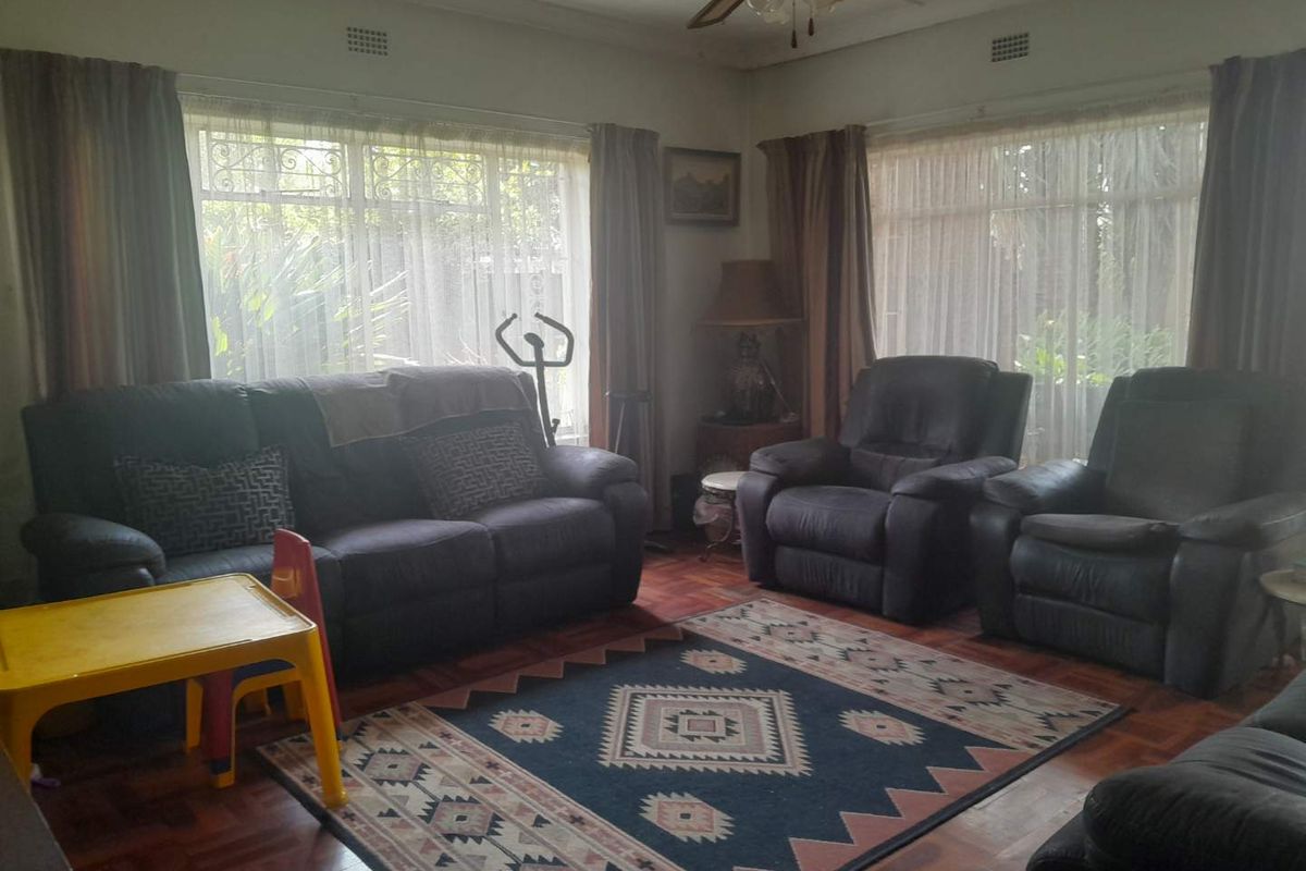 A living room featuring traditional parquet flooring, ceiling fan, and large windows with security bars, offering a classic foundation for updates.
