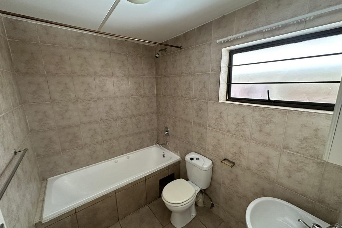 A functional bathroom featuring a built-in bathtub, toilet, and washbasin with neutral wall and floor tiling throughout.