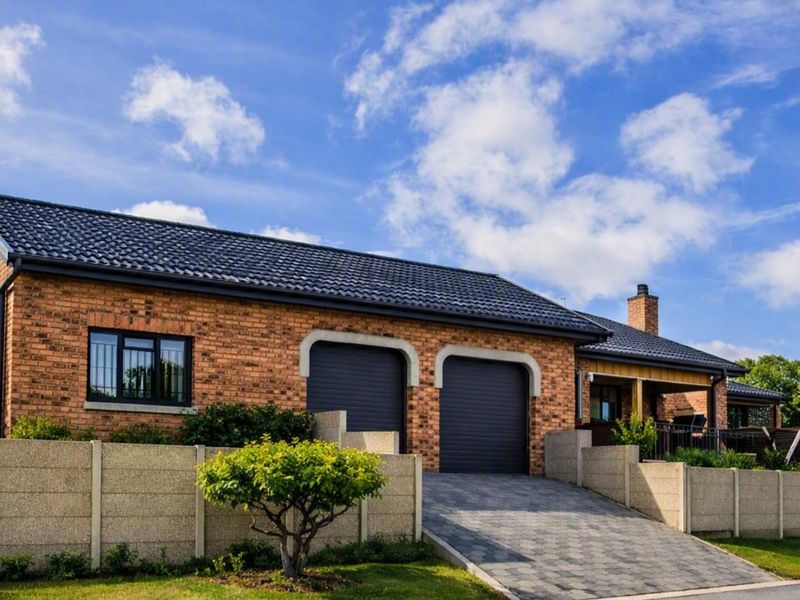 A well-maintained single-story brick house featuring a double garage, paved driveway, and secure precast boundary wall under a dark tiled roof.