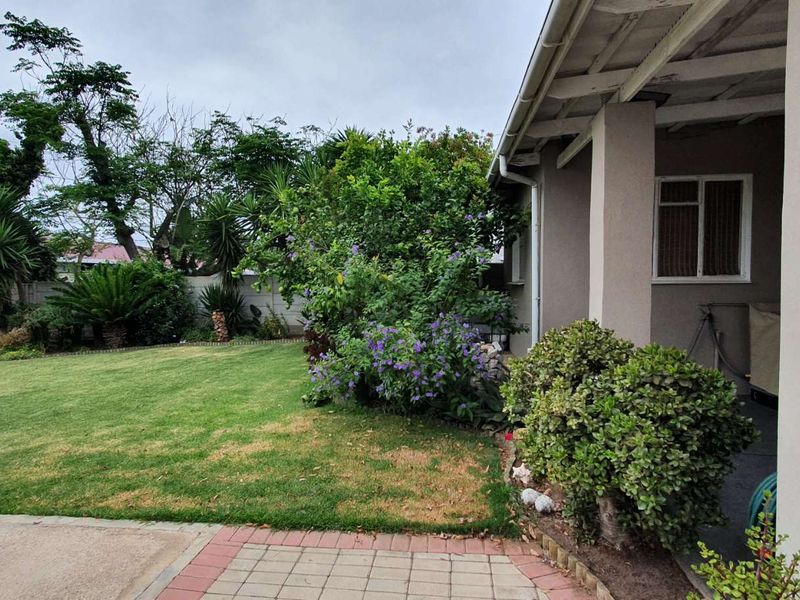 A view of the rear garden featuring a covered patio, paved walkway, and established lawn area with boundary walling.