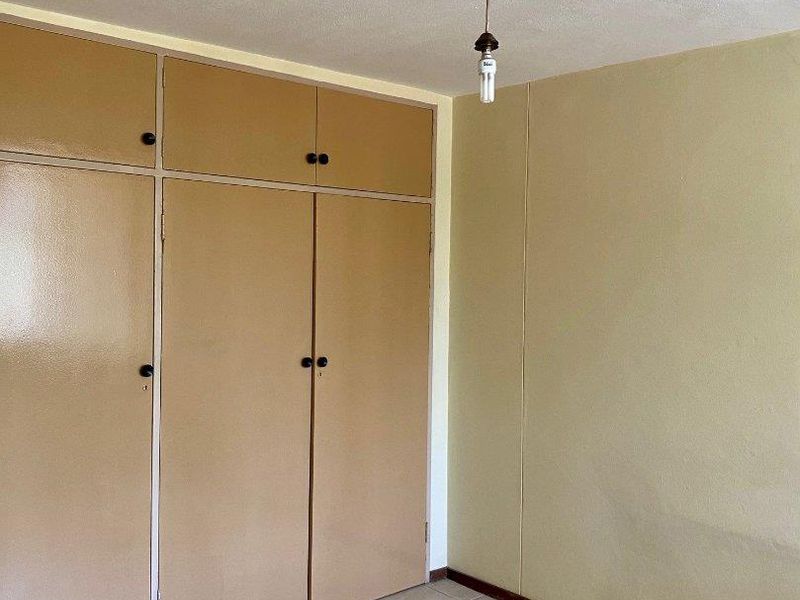 An empty bedroom featuring tiled flooring and built-in cupboards with a dated finish, offering a blank canvas for renovation.