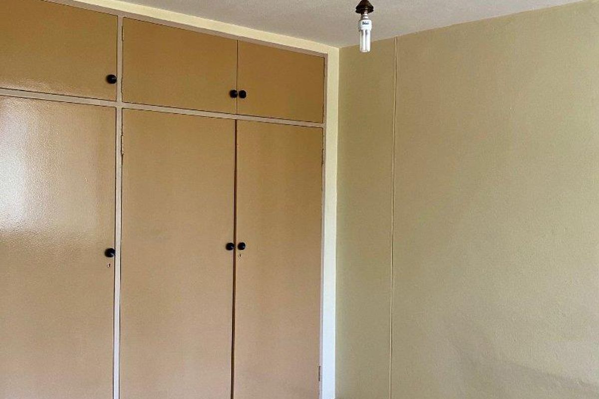 An empty bedroom featuring tiled flooring and built-in cupboards with a dated finish, offering a blank canvas for renovation.