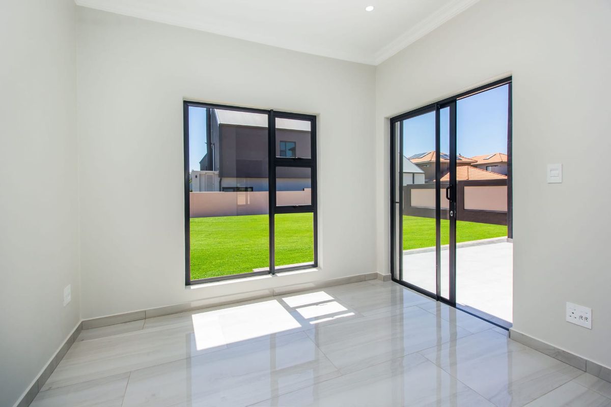 A bright, empty living area featuring modern porcelain floor tiles, large aluminium-framed windows, and sliding glass doors opening to a private garden.