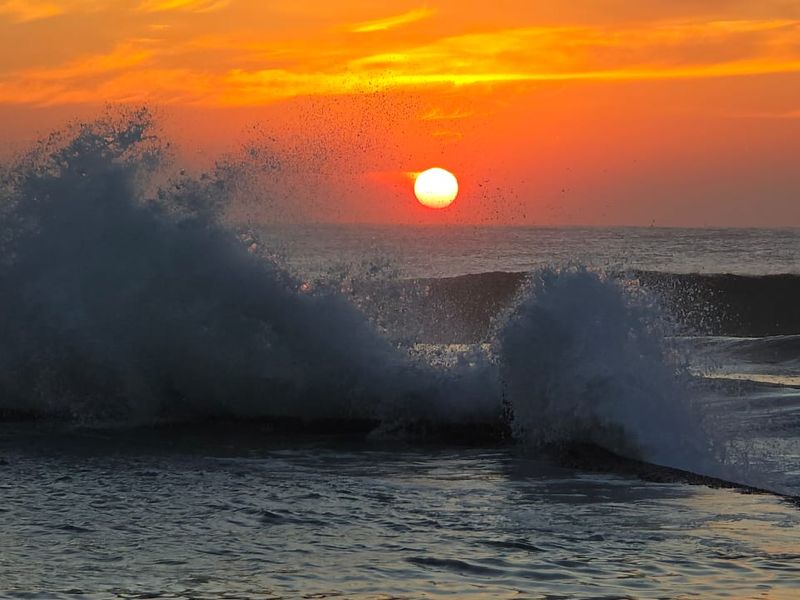 A scenic view of the ocean at sunset with waves crashing against a coastal structure.
