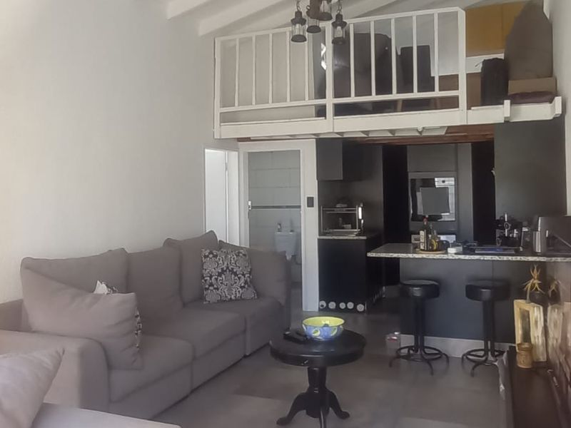 Open-plan living area featuring a mezzanine level, exposed beam ceilings, tiled flooring, and a modern kitchen with a breakfast bar.
