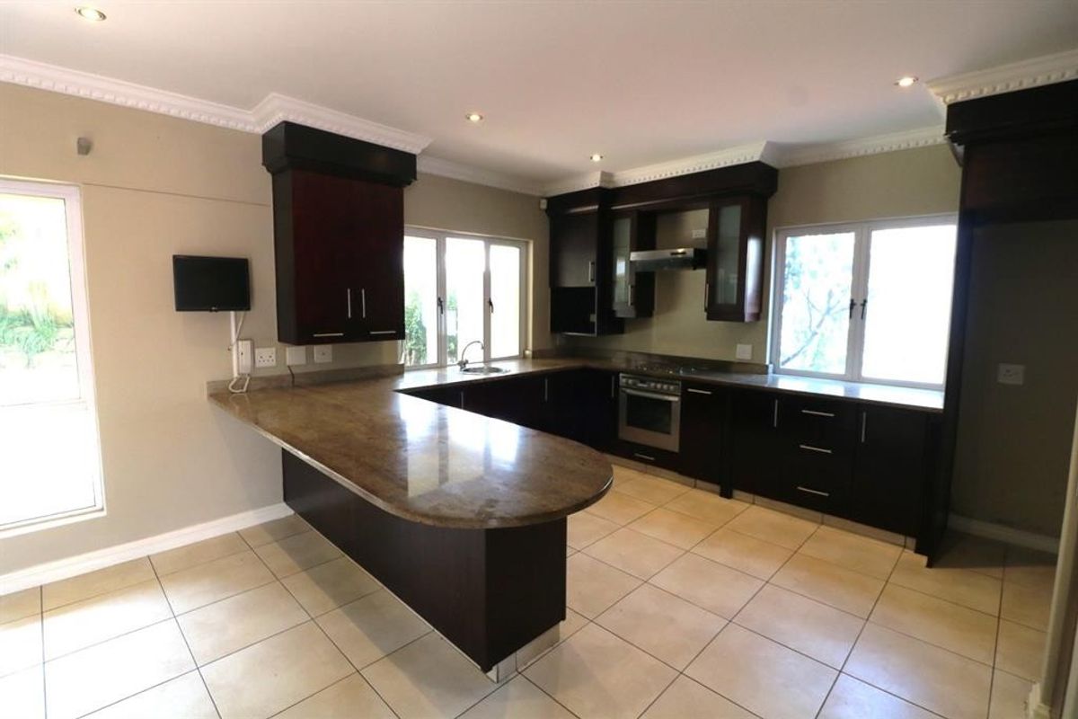Spacious kitchen featuring dark wood cabinetry, stone countertops with a breakfast bar, built-in oven, extractor fan, and tiled flooring.