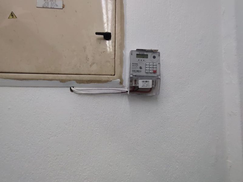 A utility wall featuring a mounted electrical distribution board and a prepaid electricity meter.